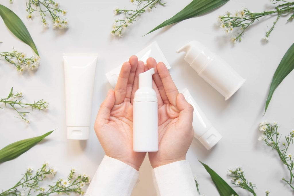 Beauty natural skincare products development concept. Dermatologist hands holding blank cosmetic skincare bottle w/ pump dispenser and organic ingredient on white background. Top view. Close up.